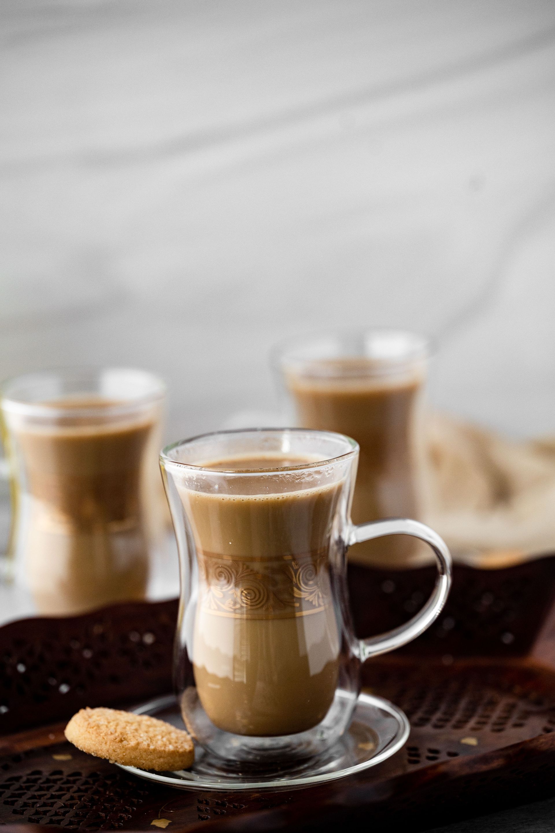 Three transparent glass cups of Turkish coffee with biscuits on a wooden tray.
