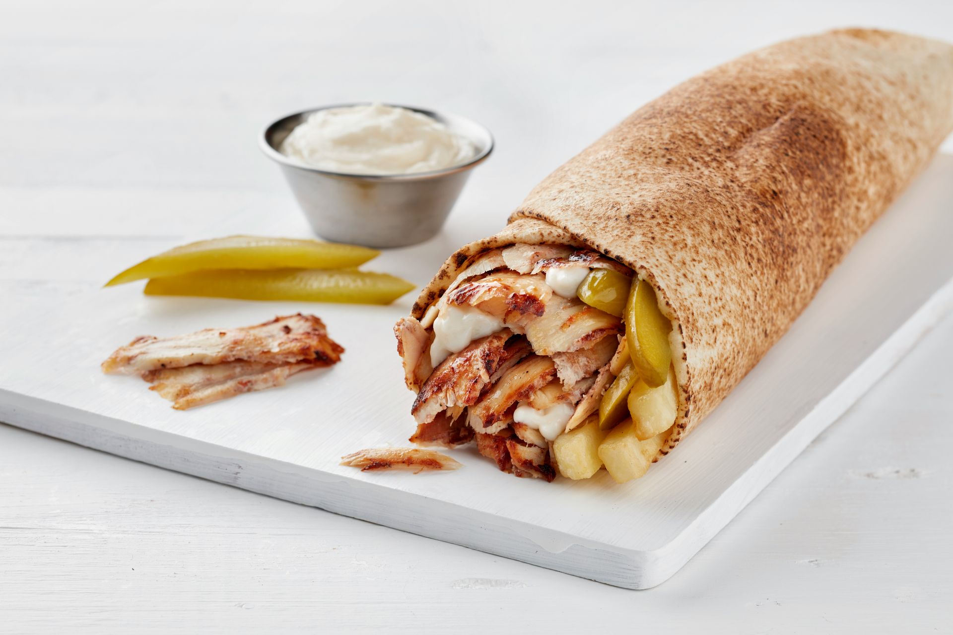 a burrito with a side of pickles and a small bowl of ranch dressing