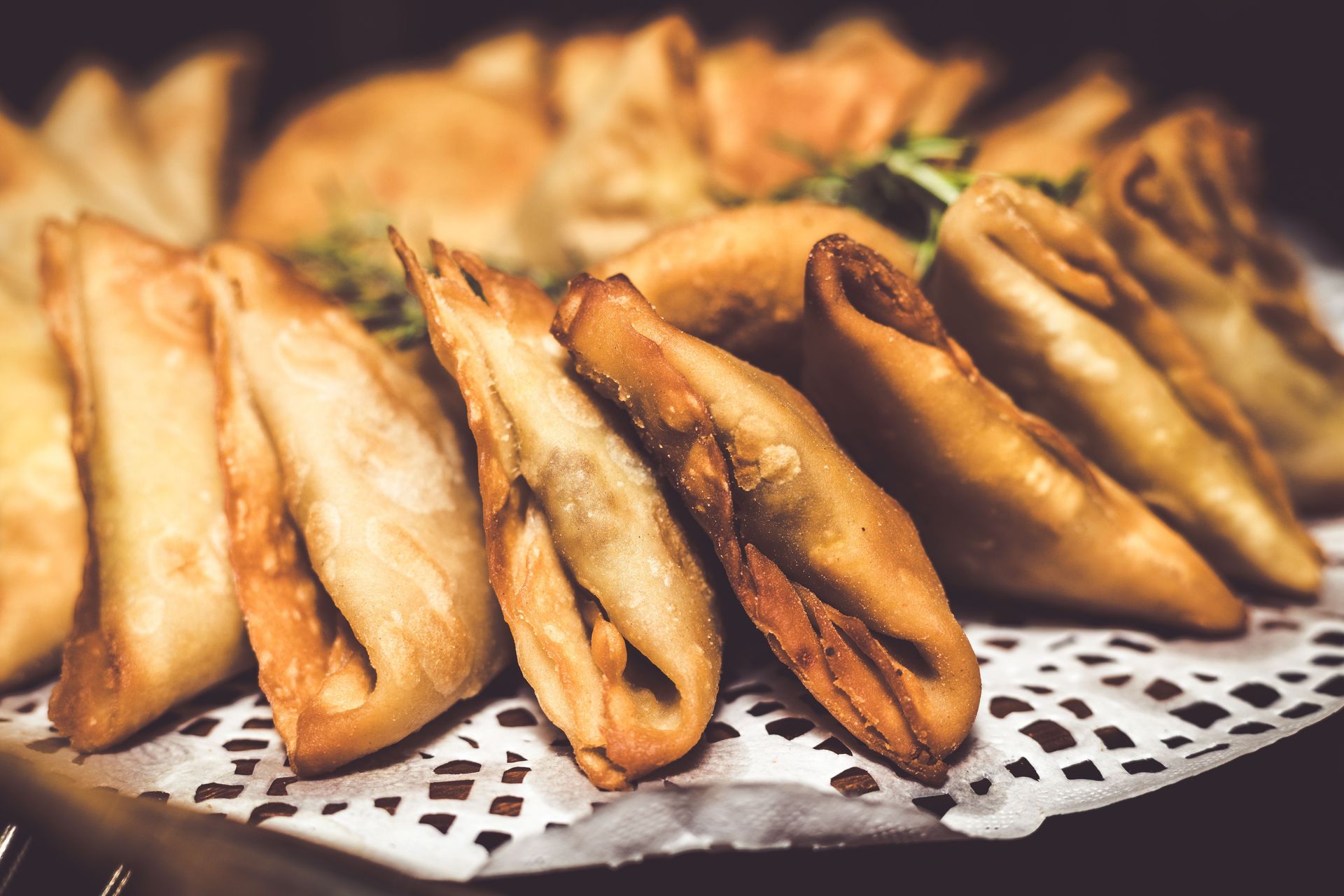 Close-up view of golden, crispy samosas arranged on a plate with a lace doily, ready to serve.